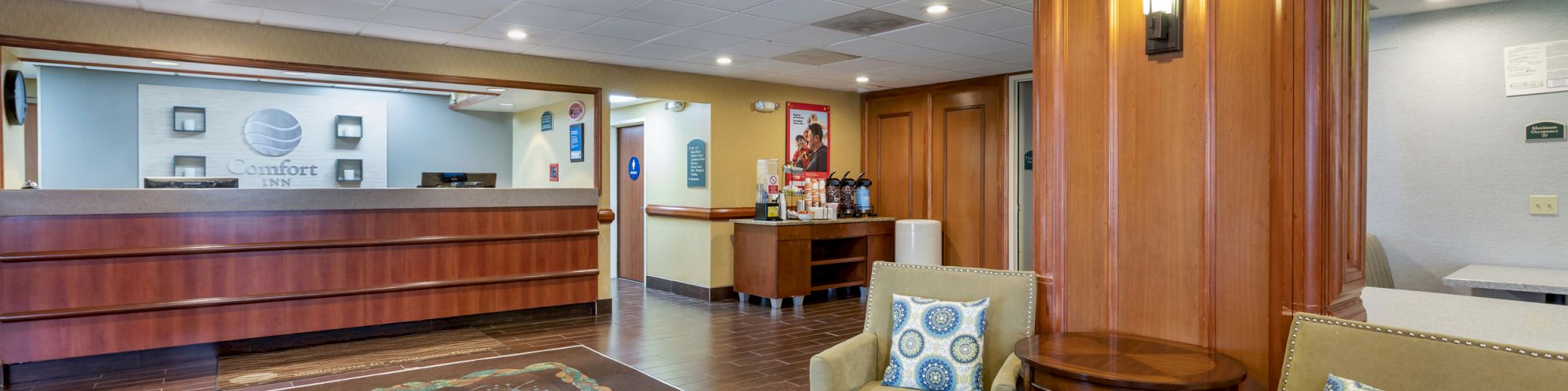 A hotel lobby with a reception desk, seating area with two chairs and a small table, and wall décor.