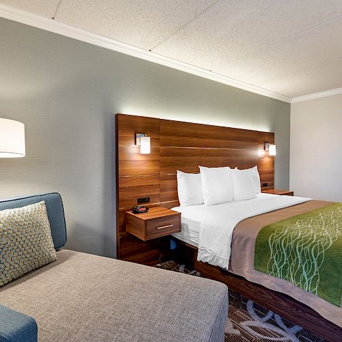 A hotel room with a bed, nightstands, and a reading chair with a floor lamp beside it, decorated in neutral tones with green accents.