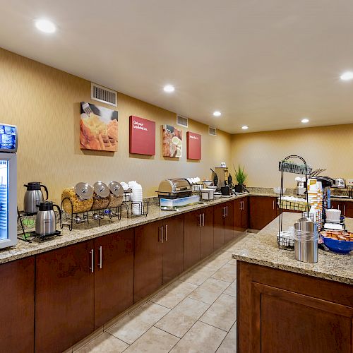 Image of a well-lit hotel breakfast buffet area with coffee dispensers, cereal, and various food items on a long counter.