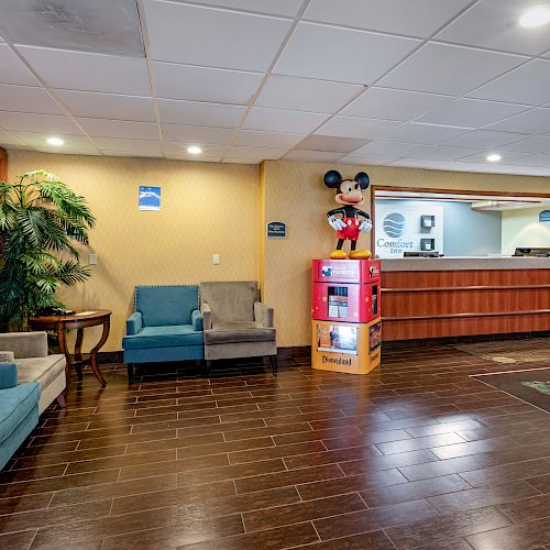 A hotel lobby with chairs, a plant, a reception desk, and a stand with a Mickey Mouse figure, having a clean, welcoming look.