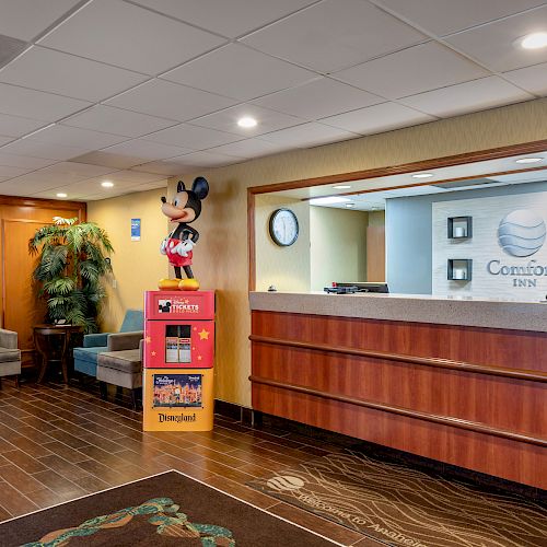 This image shows the reception area of a Comfort Inn, with a seating area, a large plant, a Mickey Mouse statue, and a front desk with computers.