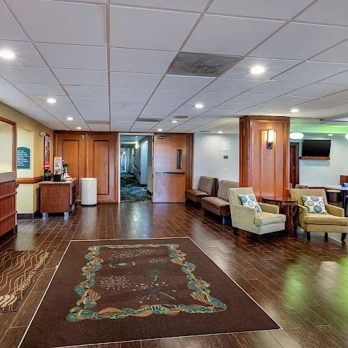 A hotel lobby with a reception desk, seating area, wall art, and television, featuring modern decor in a well-lit space.