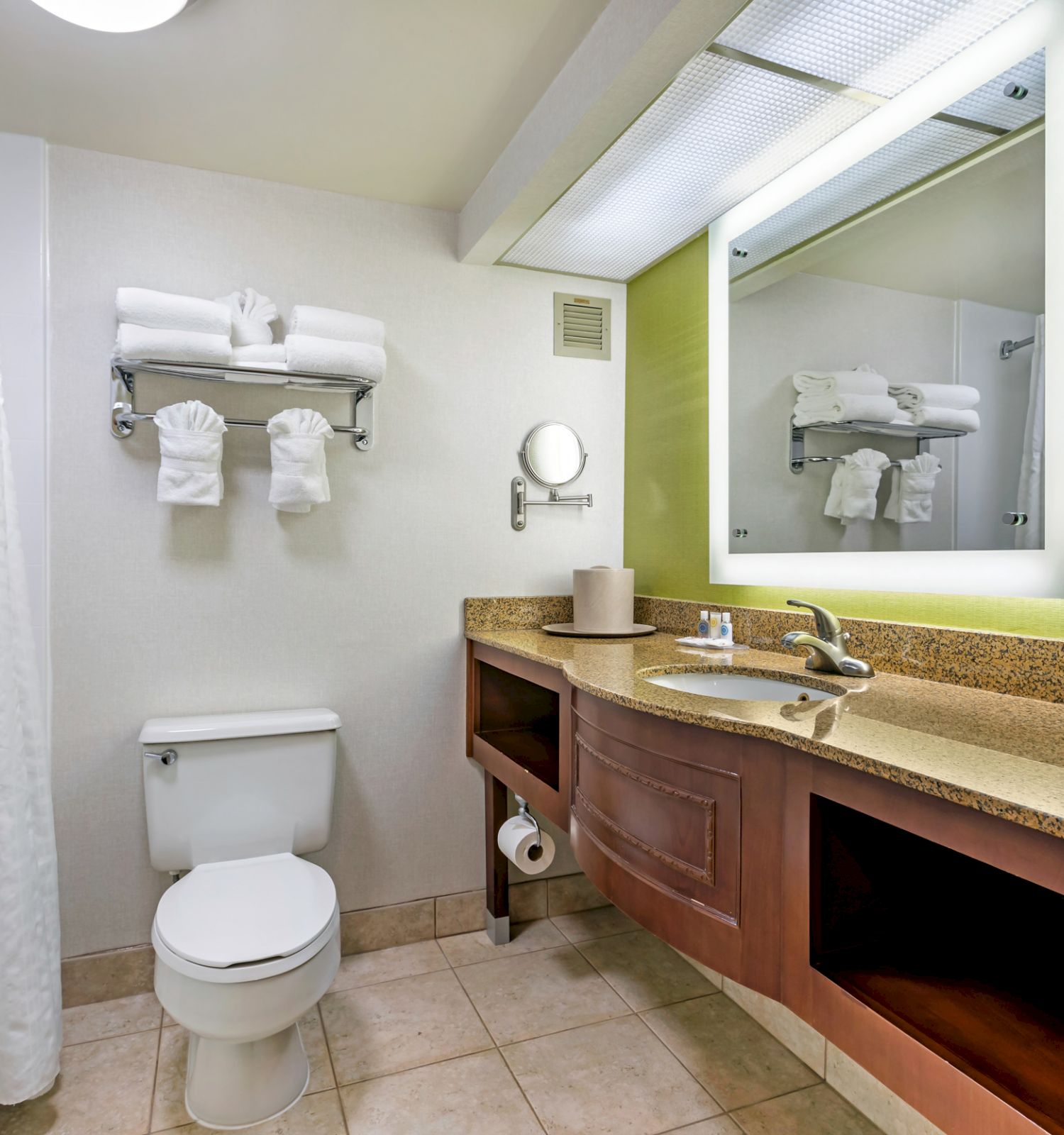 A clean, modern bathroom with a bathtub, toilet, towels, large mirror, sink with counter space, and beige tiled floor.