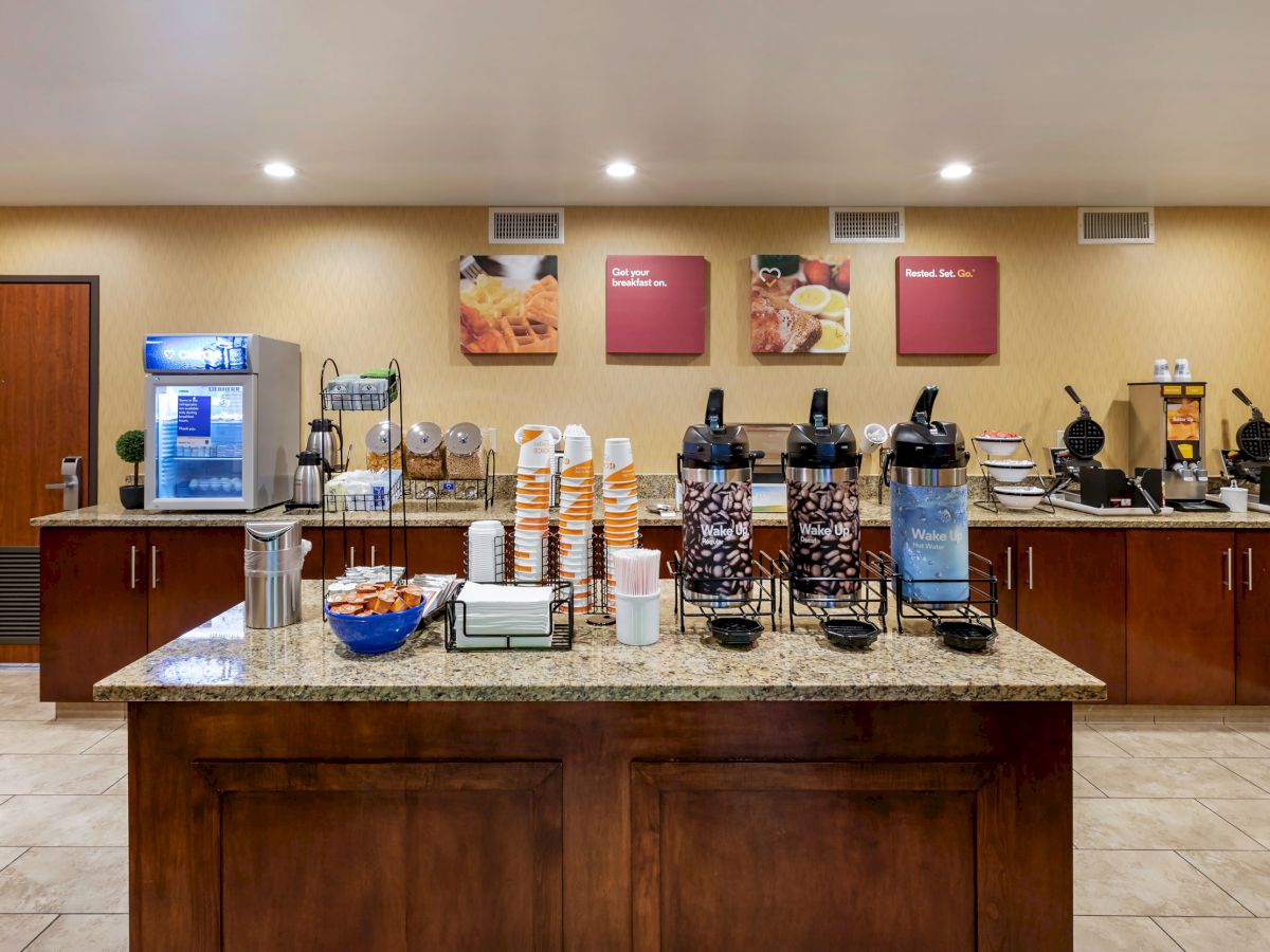 A hotel breakfast buffet featuring coffee dispensers, cups, an ice machine, and various breakfast items on a counter.