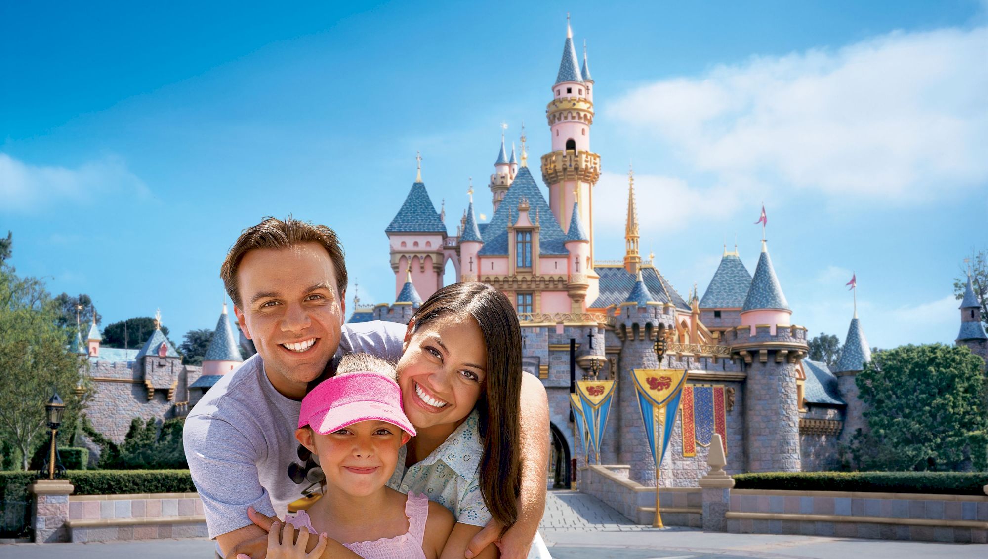 A happy family posing in front of a well-known castle at a theme park under a clear blue sky.